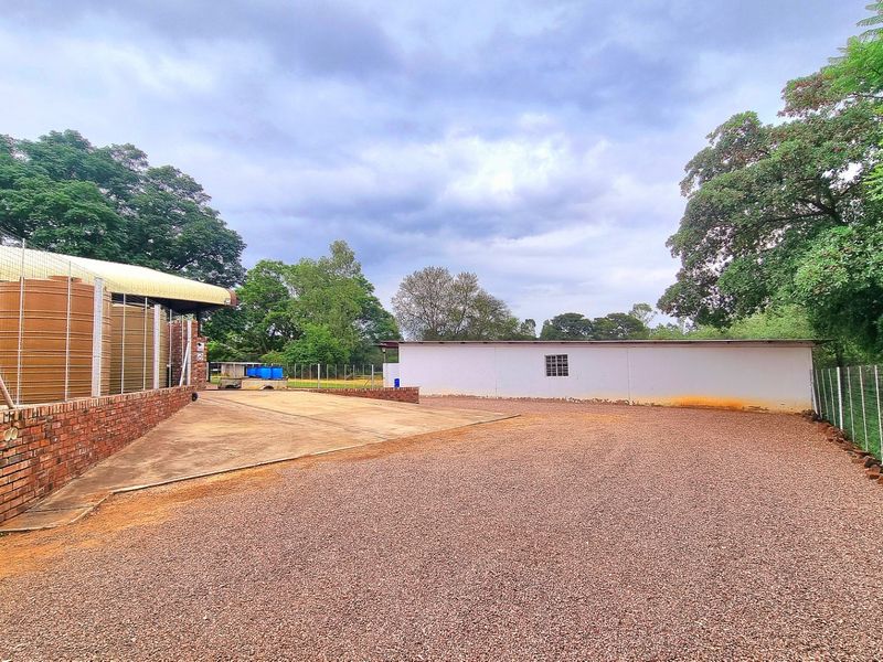 Rear farm yard area featuring a gravel driveway, brick retaining wall, water storage tanks, and a functional outbuilding with wire mesh perimeter fencing.