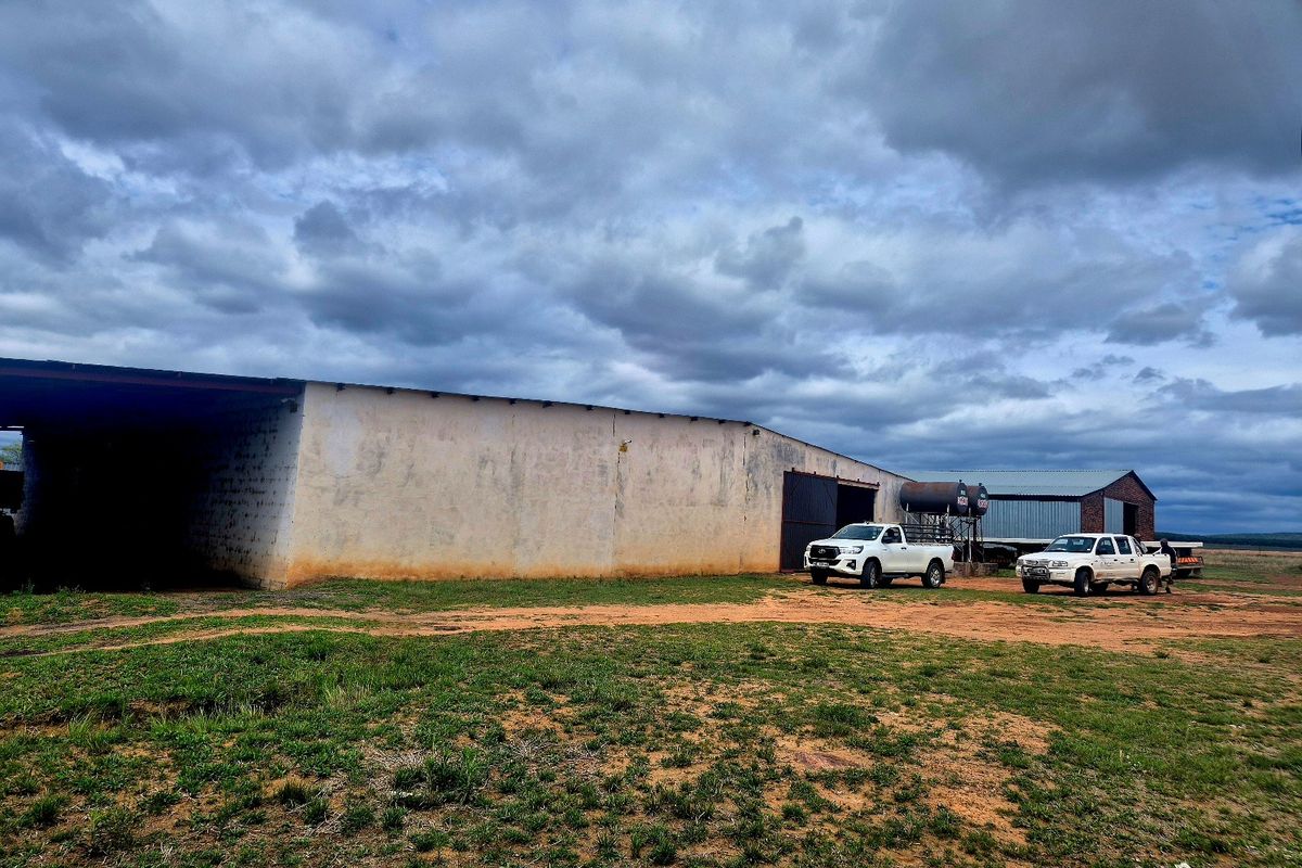 A large agricultural storage shed on a farm property, featuring metal roofing and weathered exterior walls, set within an open rural landscape.