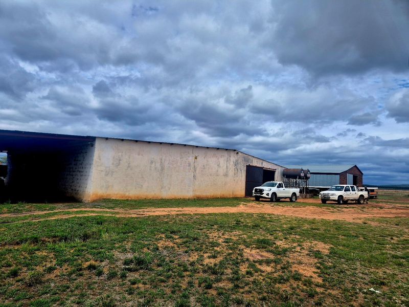 A large agricultural storage shed on a farm property, featuring metal roofing and weathered exterior walls, set within an open rural landscape.