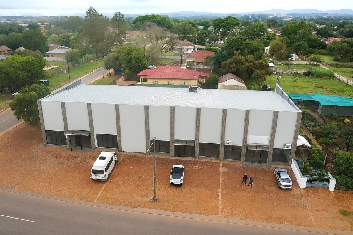 Aerial view of a commercial building featuring a metal roof, multiple glass storefront entrances, and an adjacent paved parking area.