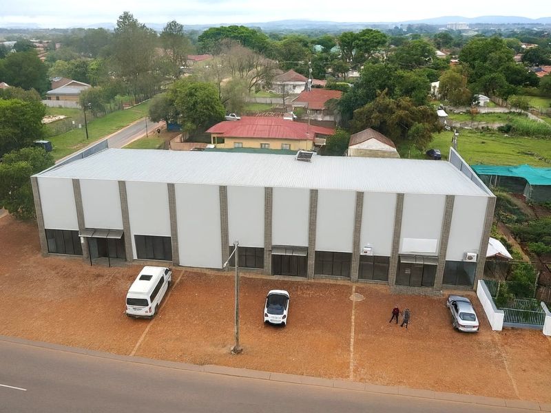 Aerial view of a commercial building featuring a metal roof, multiple glass storefront entrances, and an adjacent paved parking area.