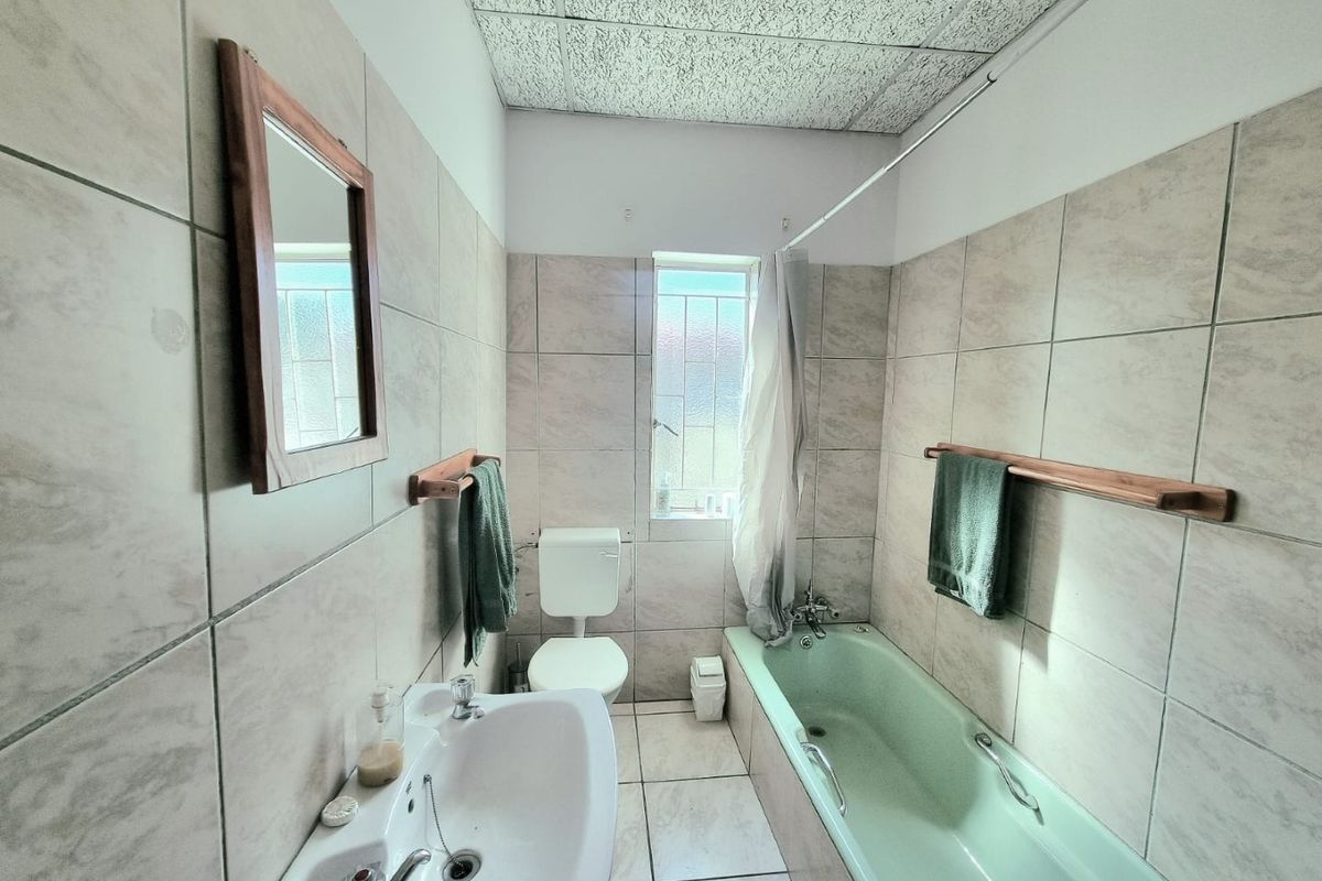A functional bathroom featuring neutral wall and floor tiling, a pedestal basin, and a classic bathtub with an integrated shower fixture.