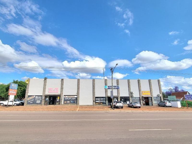 A commercial strip mall featuring multiple storefronts with paved parking access, prominent signage, and exterior air conditioning units along the main road.
