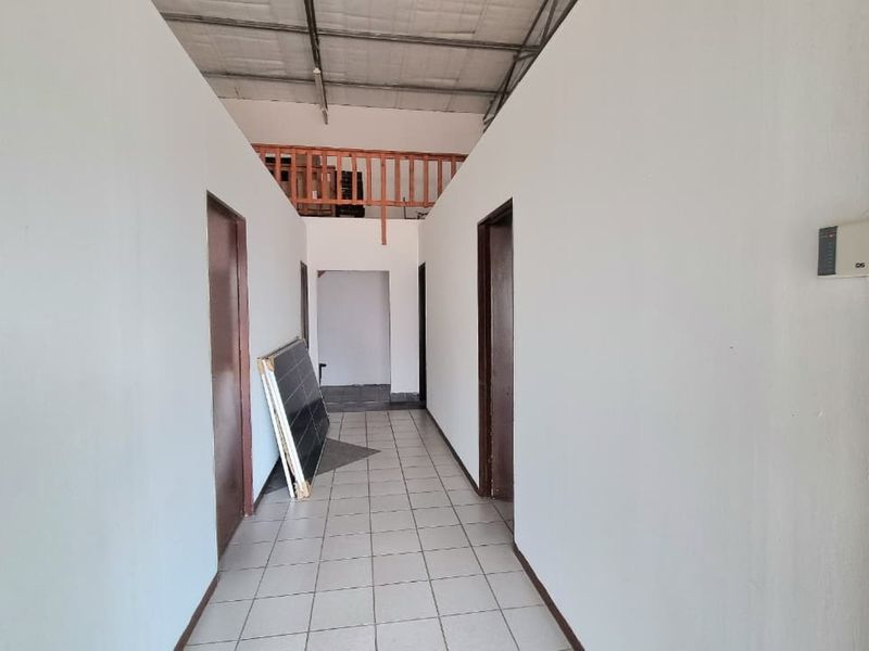 A functional commercial hallway featuring tiled flooring, neutral walls, and access to a mezzanine level with a wooden balustrade.