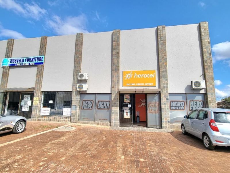 Front facade of a commercial building featuring stone-clad pillars, glass storefronts, and dedicated paved parking space.