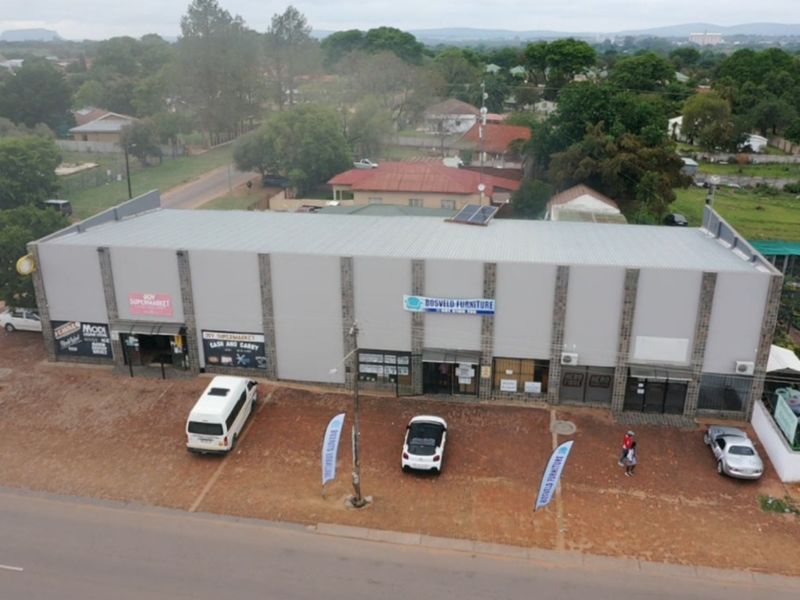 Aerial view of a commercial retail building featuring a metal roof with solar panels, stone-clad pillars, and an adjacent paved parking area.