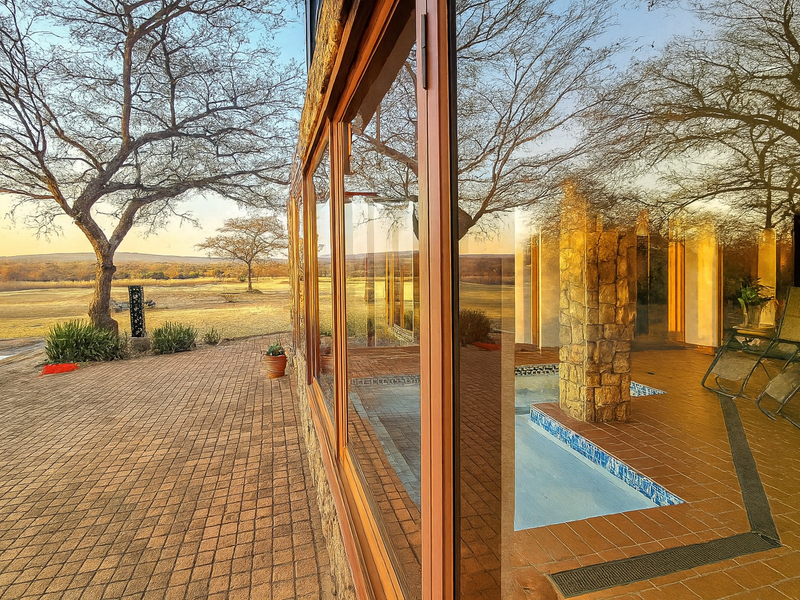 A covered patio area featuring tiled flooring, a stone-clad pillar, and a built-in pool, offering seamless indoor-outdoor flow with expansive glass views.
