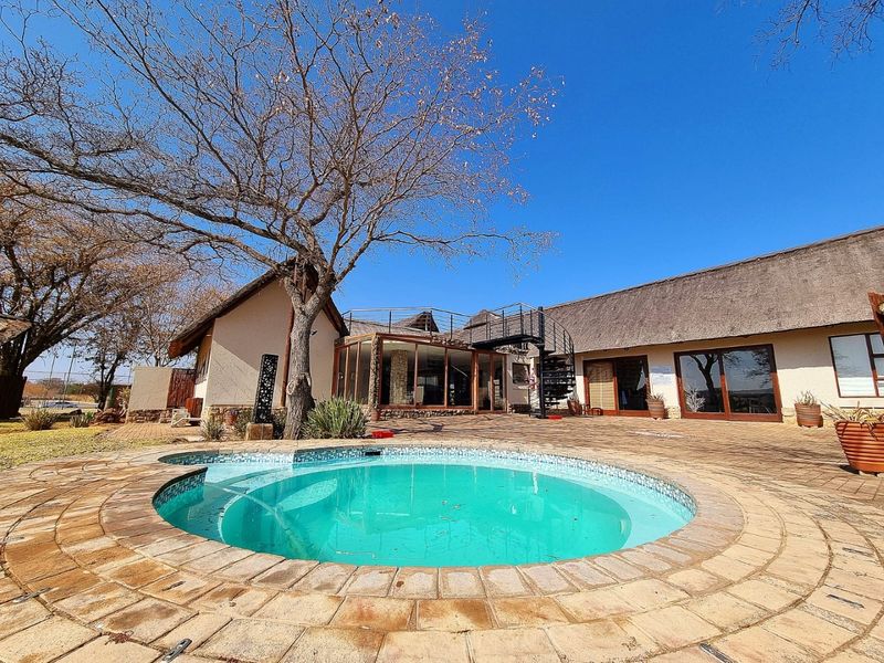 Outdoor pool area featuring a circular swimming pool, paved patio, thatched roof architecture, and an external spiral staircase leading to an upper level.