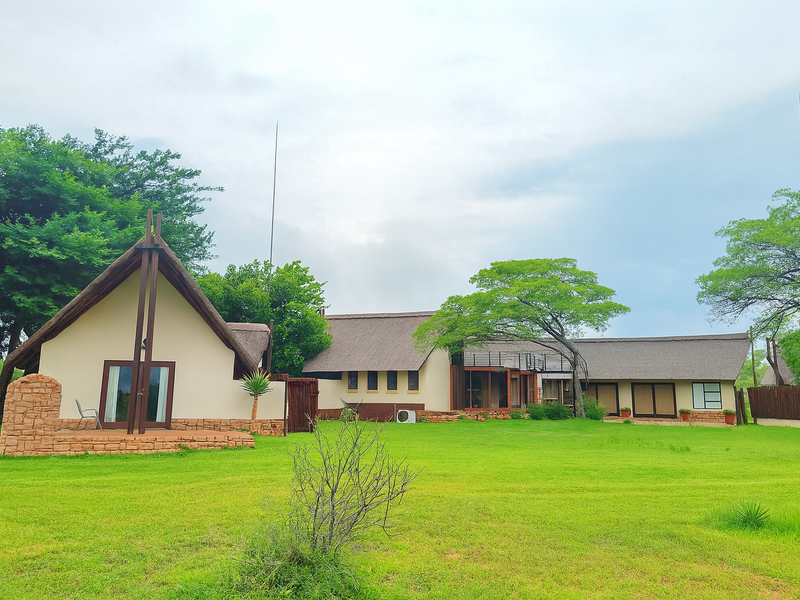 A spacious rear view of a property featuring traditional thatched roofing, stone accents, and expansive green lawns in a tranquil setting.