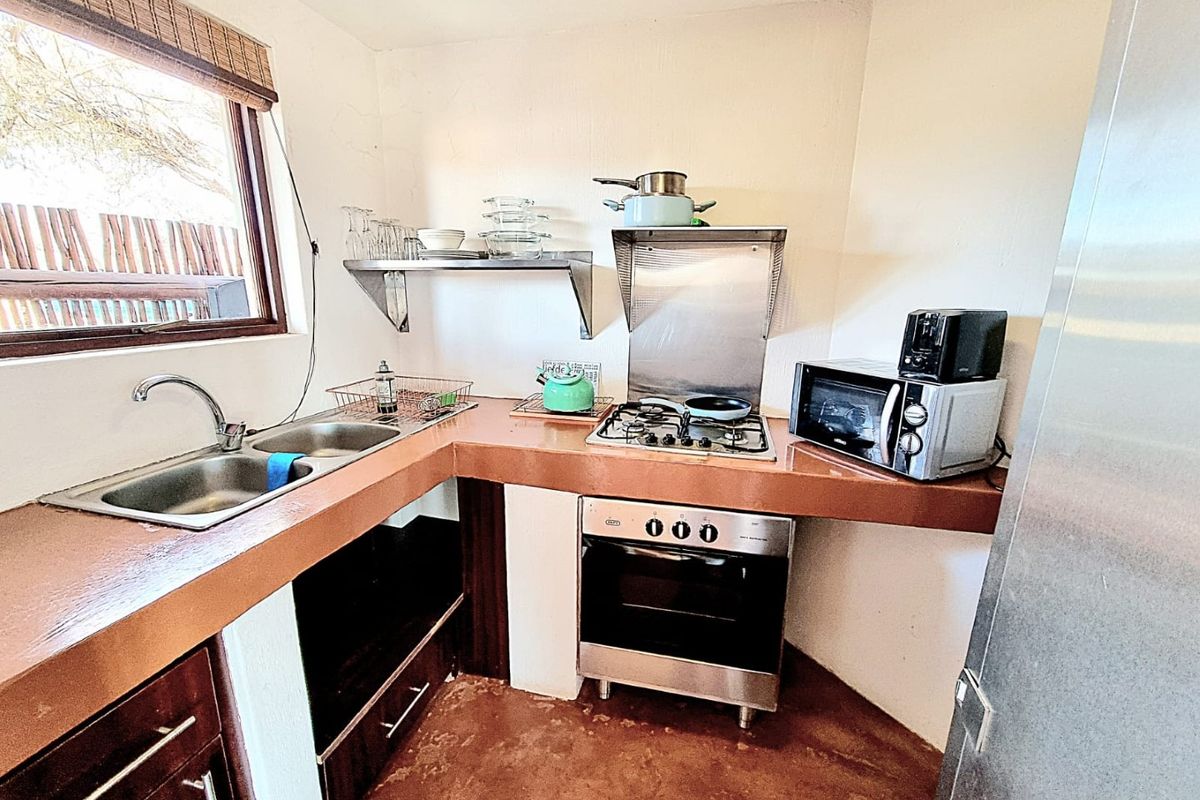 Compact kitchen featuring a double bowl sink, gas hob, built-in oven, stainless steel extractor, and wall-mounted shelving with tiled countertops.