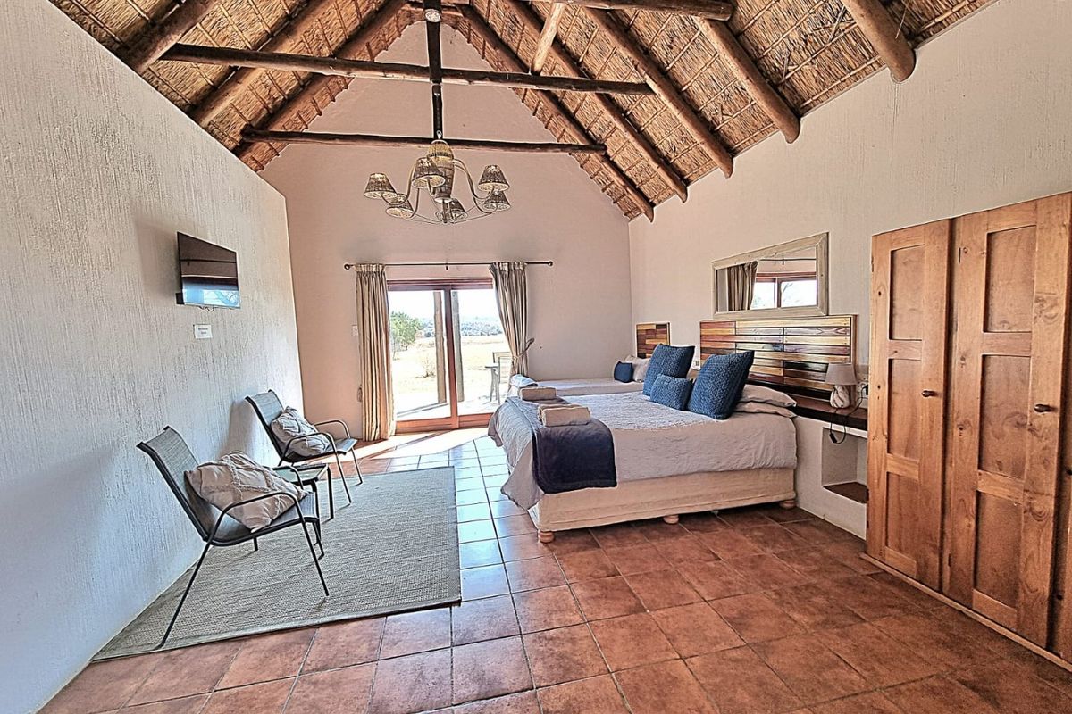 Spacious bedroom featuring a high vaulted thatched ceiling with exposed timber trusses, terracotta tiled flooring, and direct access to the outdoors via sliding doors.