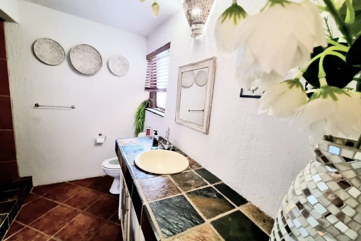 A bathroom featuring a tiled vanity with a vessel sink, tiled flooring, and a toilet, finished with textured walls and wooden blinds.