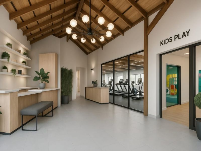 Modern clubhouse lobby featuring a vaulted timber ceiling, feature chandelier, built-in reception counter, and glass-partitioned access to the gym and kids play area.