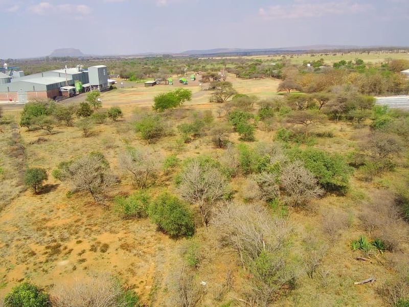 Aerial view of a large commercial vacant land plot featuring an industrial facility with silos and a fenced storage area.