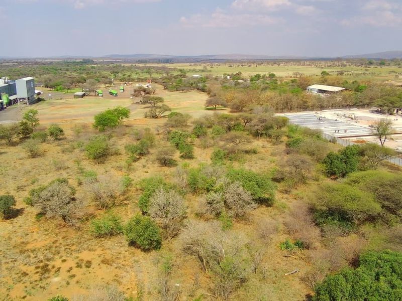 Aerial view of a large commercial vacant land plot featuring existing industrial structures and surrounding natural vegetation.