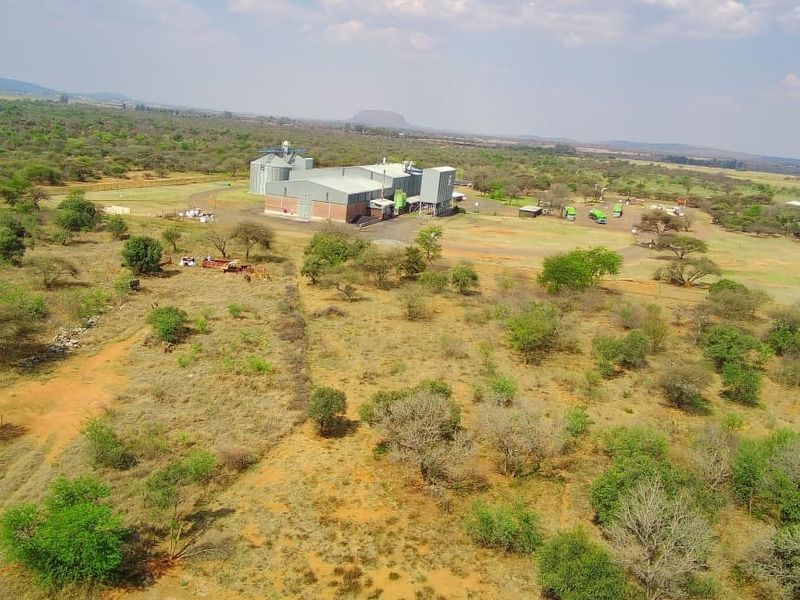 Aerial view of a commercial vacant land property featuring an industrial warehouse facility and grain silos set within a large rural landscape.