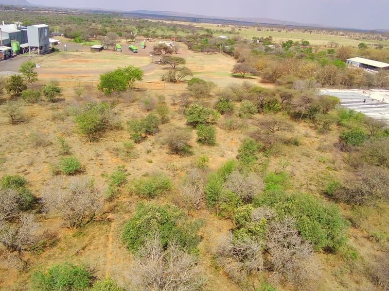 Aerial view of a large, undeveloped commercial land parcel featuring native vegetation, adjacent to an existing industrial facility and access roads.