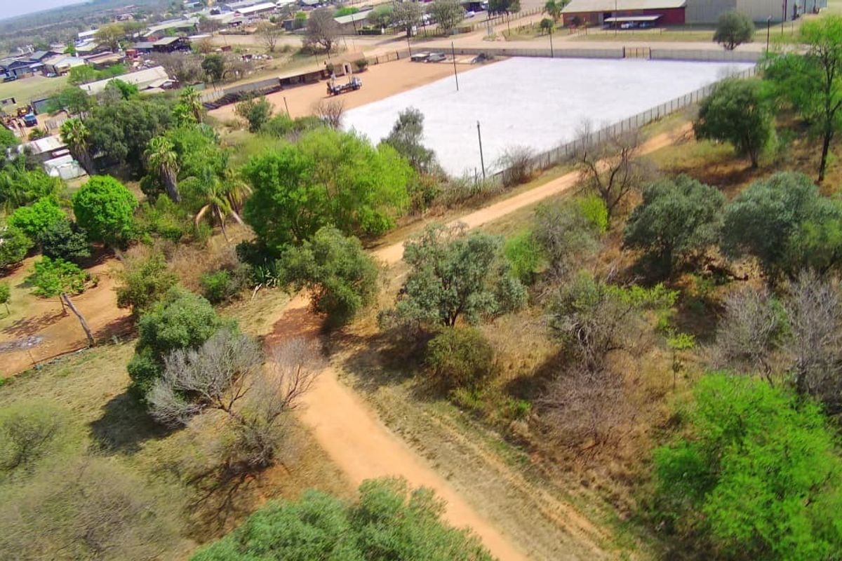 Aerial view of a commercial vacant land plot featuring cleared areas, fencing, and access via a dirt road in a semi-rural setting.
