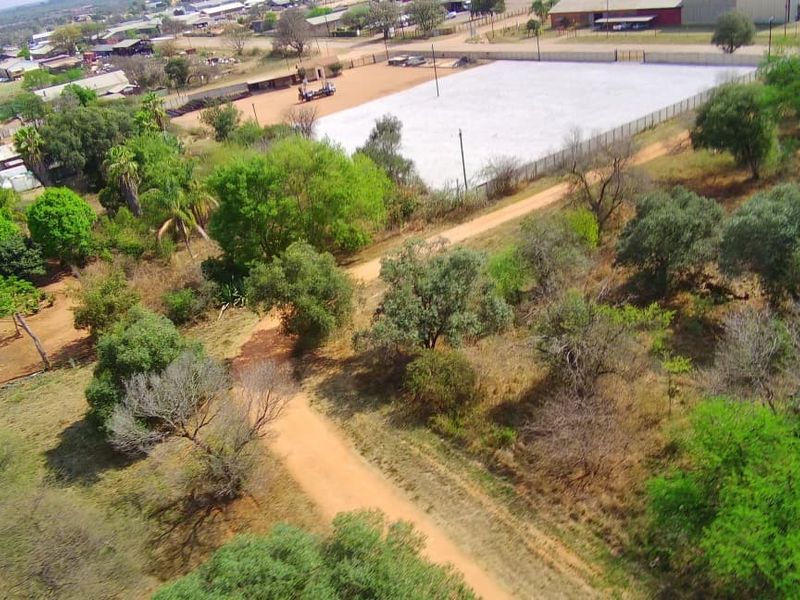 Aerial view of a commercial vacant land plot featuring cleared areas, fencing, and access via a dirt road in a semi-rural setting.