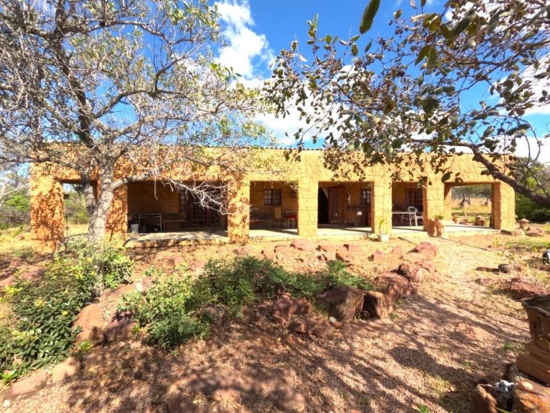 A rustic farm-style dwelling featuring a covered patio with stone pillars and masonry walls, set within a natural, rocky landscape.