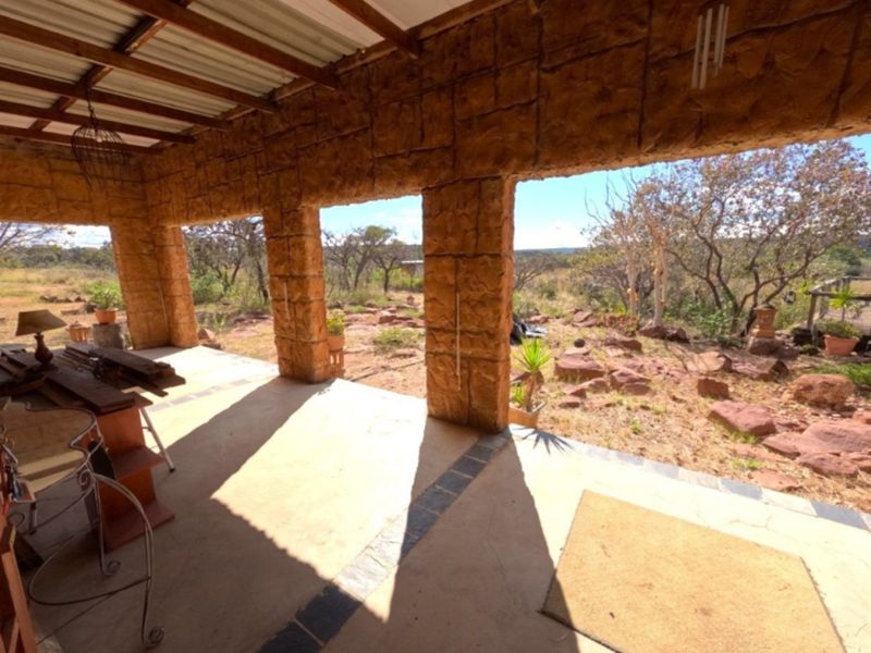 A rustic covered patio featuring stone masonry pillars, exposed timber rafters, and a corrugated metal roof, overlooking the surrounding farm landscape.