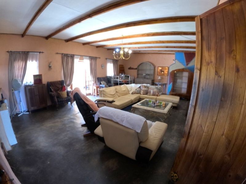 Spacious living room featuring exposed timber ceiling beams, concrete flooring, and a built-in fireplace, offering a rustic farm-style aesthetic.