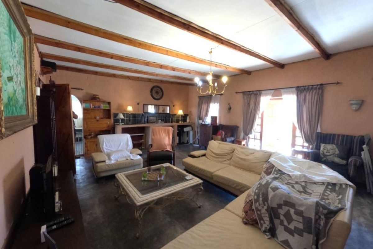 Spacious living room featuring exposed timber ceiling beams, tiled flooring, and a built-in bar area with access to the outdoors via french doors.