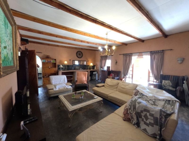 Spacious living room featuring exposed timber ceiling beams, tiled flooring, and a built-in bar area with access to the outdoors via french doors.