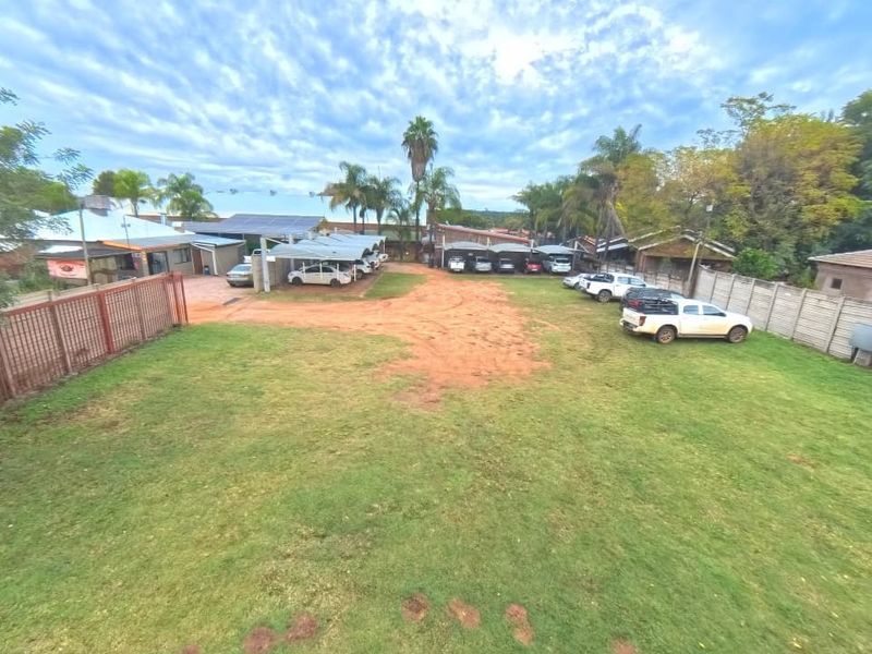 Aerial view of a commercial property featuring a large lawn, paved driveway, multiple carport structures, and secure perimeter walling.
