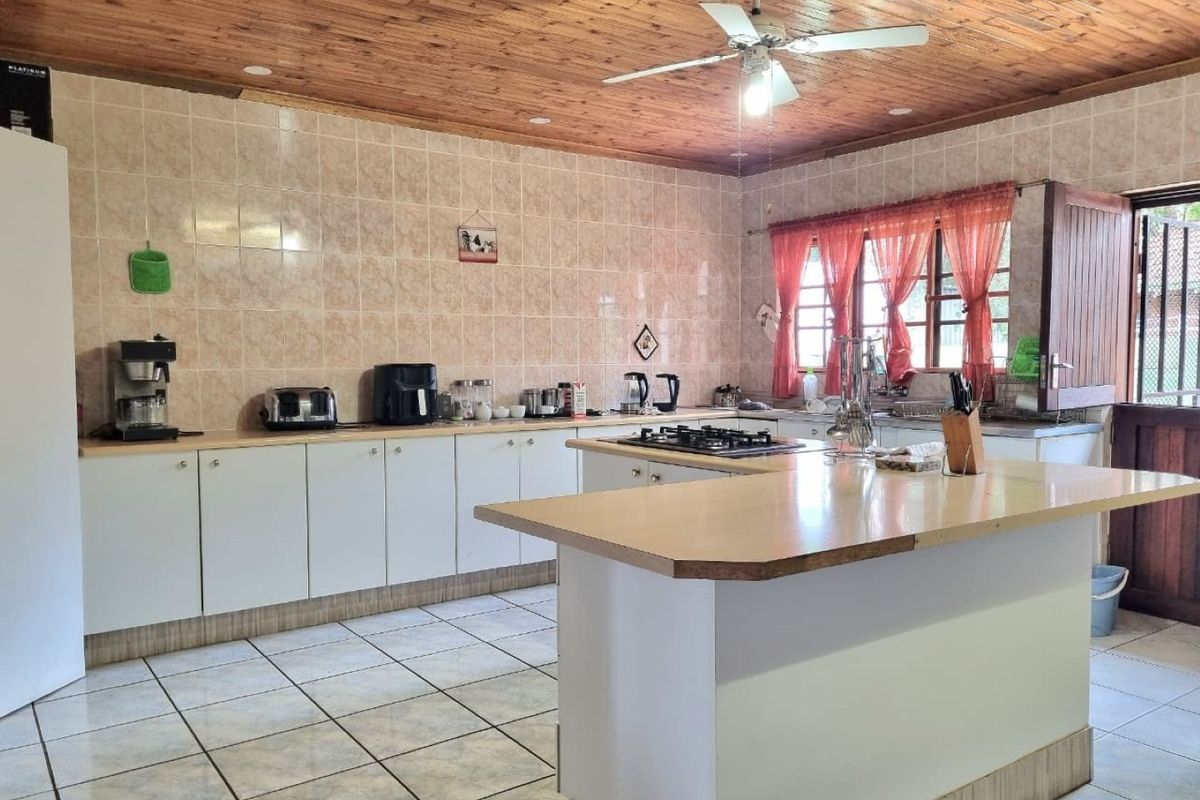 Spacious kitchen featuring a central island, gas hob, tiled backsplash, and a distinctive timber ceiling with a built-in fan.