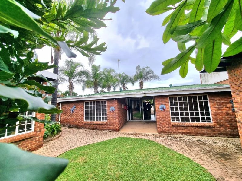 A rear view of a commercial brick building featuring a paved courtyard, green lawn, and sliding glass door entrance.