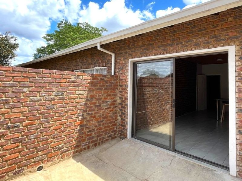 Rear exterior view of the flat featuring a face brick facade, concrete patio area, and a sliding glass door entrance.