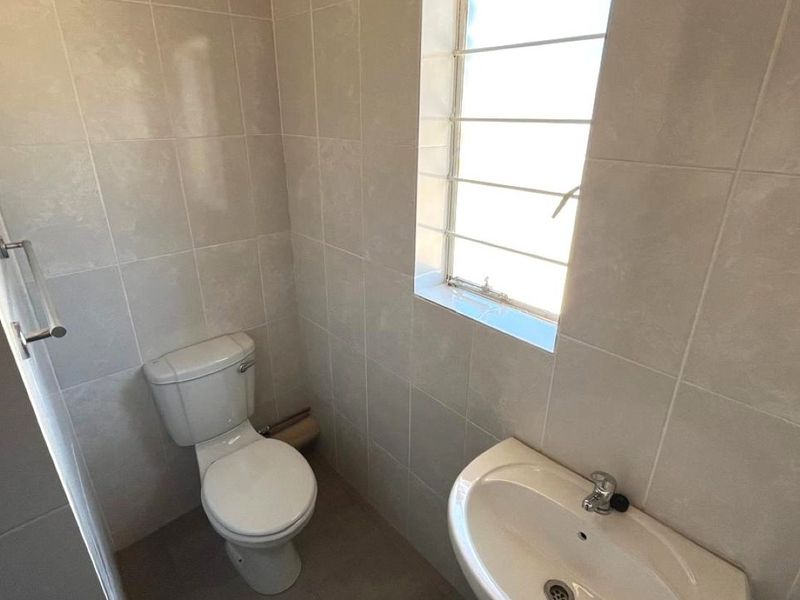 A functional bathroom featuring tiled walls, a pedestal basin, and a toilet, with a window fitted with security bars for added safety.