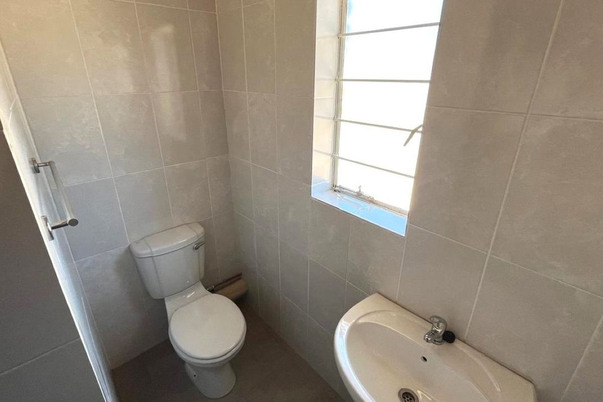 A functional bathroom featuring tiled walls, a pedestal basin, and a toilet, with a window fitted with security bars for added safety.