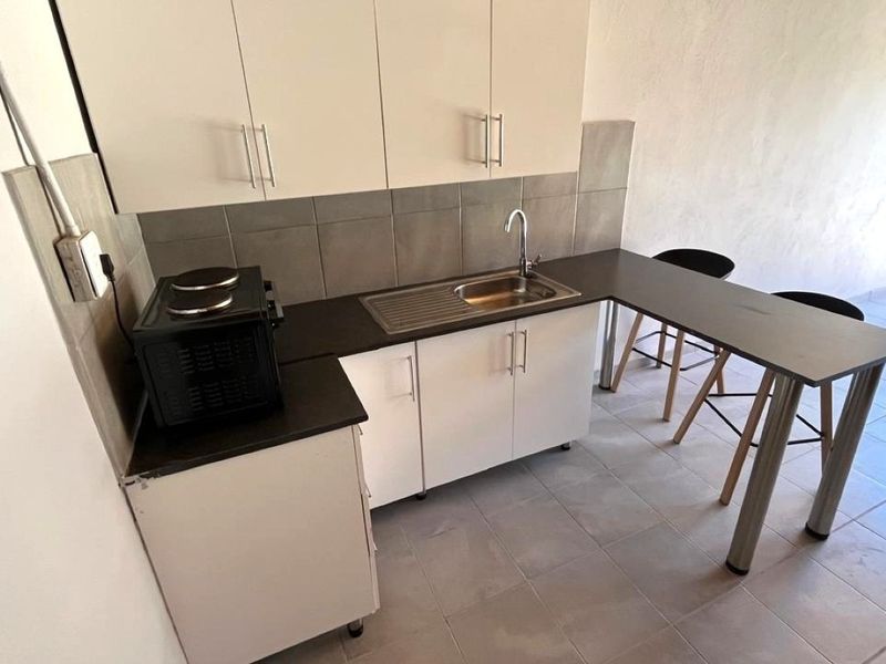 Compact kitchen featuring white cabinetry, a stainless steel sink, tiled backsplash, and an integrated breakfast bar counter.