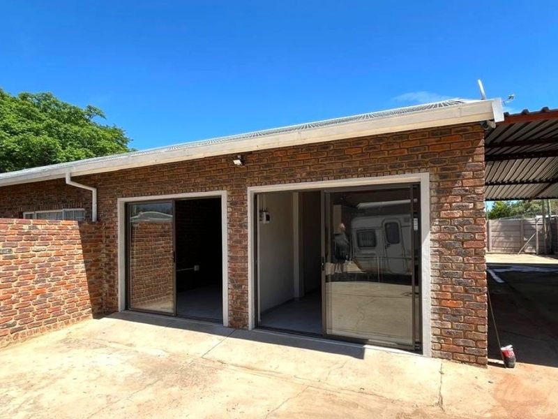 Rear exterior view of a face brick flat featuring sliding glass doors, a concrete patio area, and an adjacent carport structure.