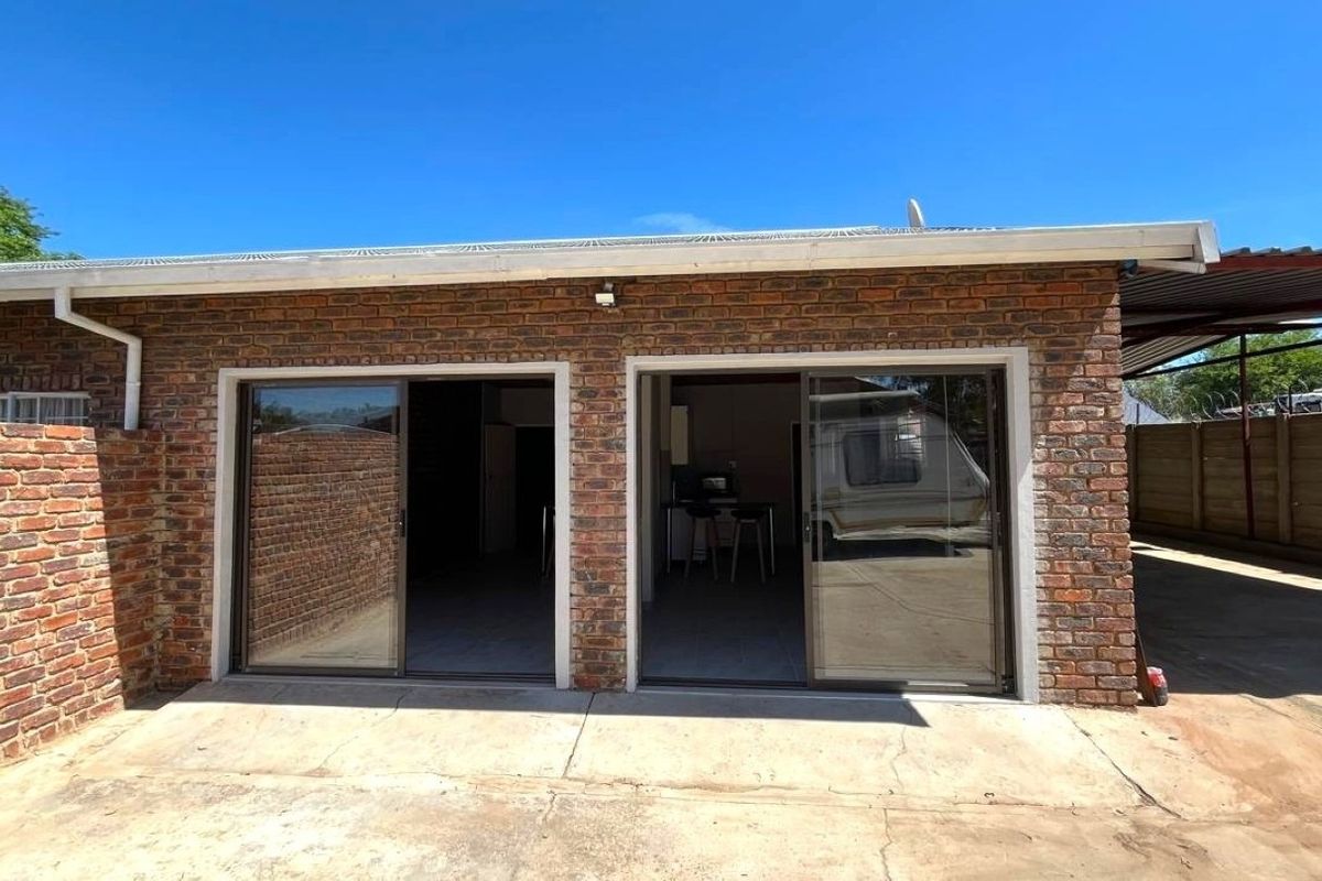 Rear exterior view of the property featuring a face brick facade, sliding glass doors, and a concrete patio area.