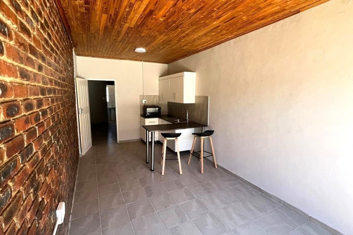 Compact kitchen area featuring exposed brickwork, a timber ceiling, tiled floors, and functional built-in cabinetry with a sink.