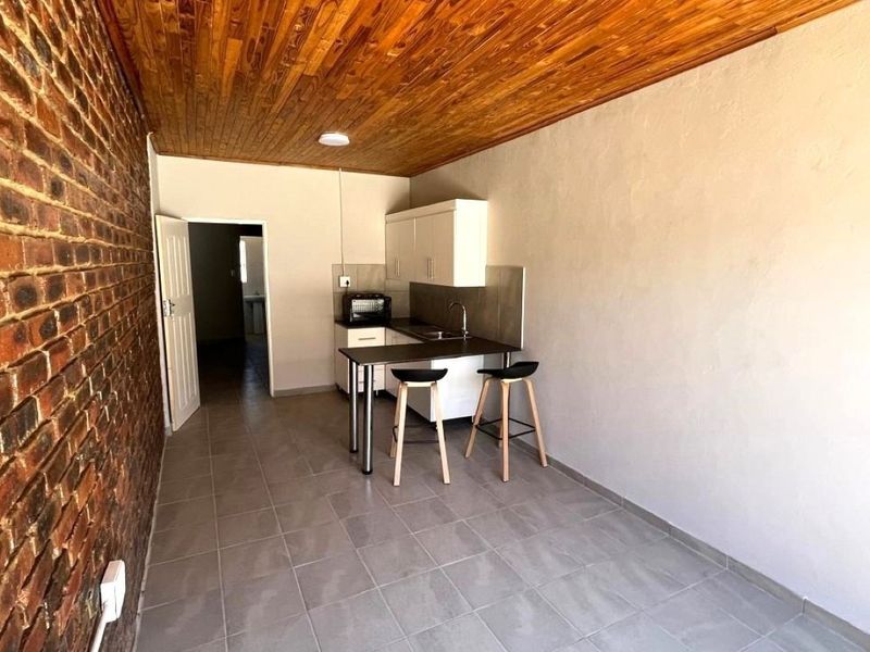 Compact kitchen area featuring exposed brickwork, a timber ceiling, tiled floors, and functional built-in cabinetry with a sink.