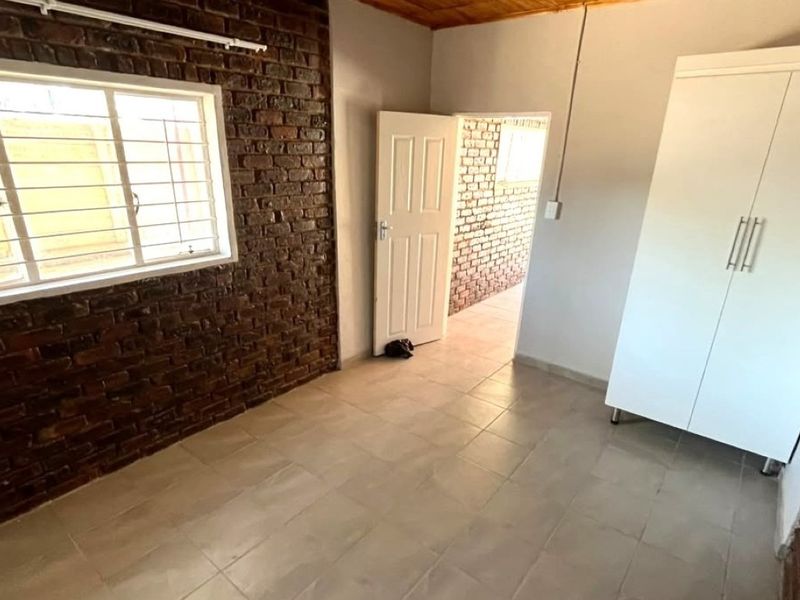 A bedroom featuring exposed brick walls, tiled flooring, and a timber ceiling, with a window fitted with security bars.