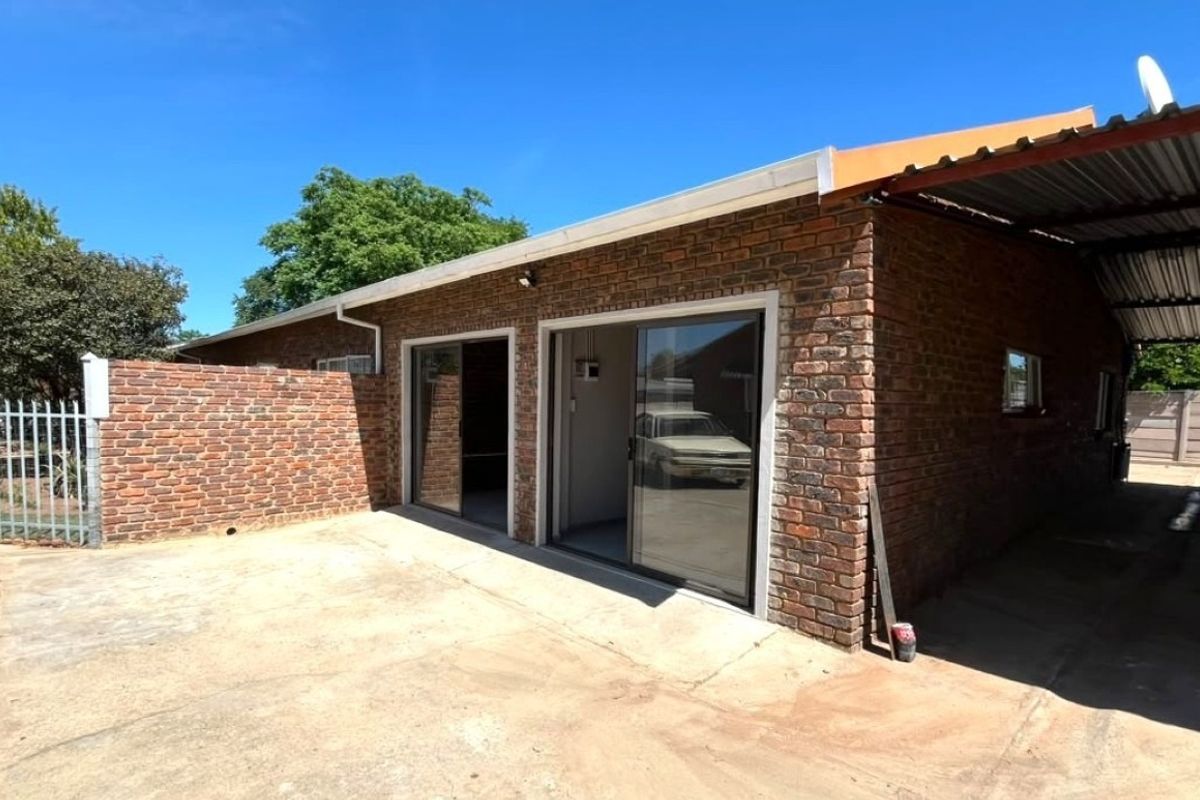 Rear view of a face brick property featuring sliding glass doors, a covered carport area, and paved outdoor space.