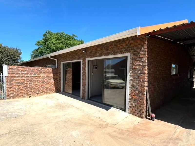 Rear view of a face brick property featuring sliding glass doors, a covered carport area, and paved outdoor space.