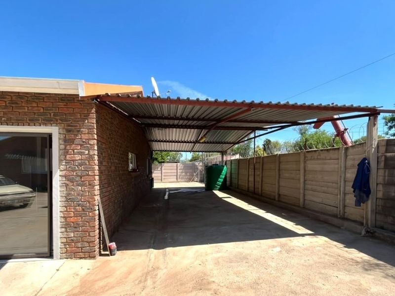 A rear exterior view featuring a covered carport, concrete driveway, and precast boundary wall, providing functional outdoor space and vehicle storage.