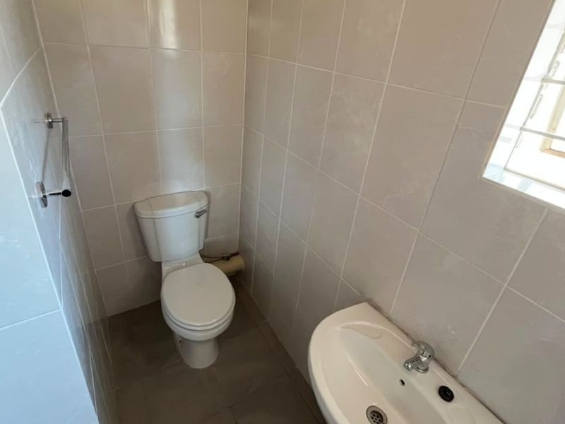 A compact bathroom featuring tiled walls and flooring, equipped with a standard toilet, washbasin, and a window with security bars.