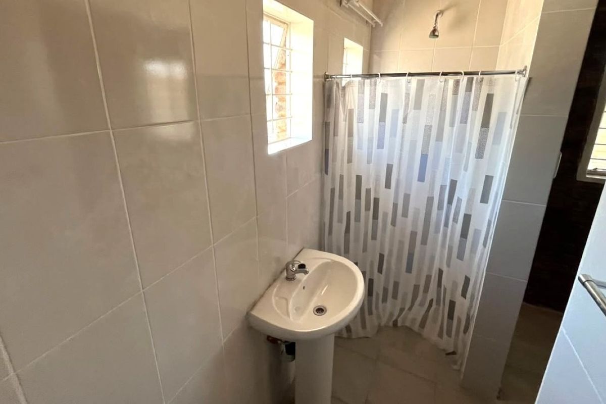 A functional bathroom featuring tiled walls and flooring, a pedestal basin, and a shower area with a curtain.