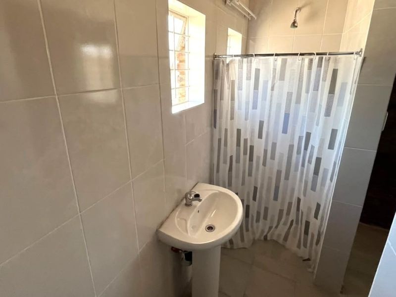 A functional bathroom featuring tiled walls and flooring, a pedestal basin, and a shower area with a curtain.
