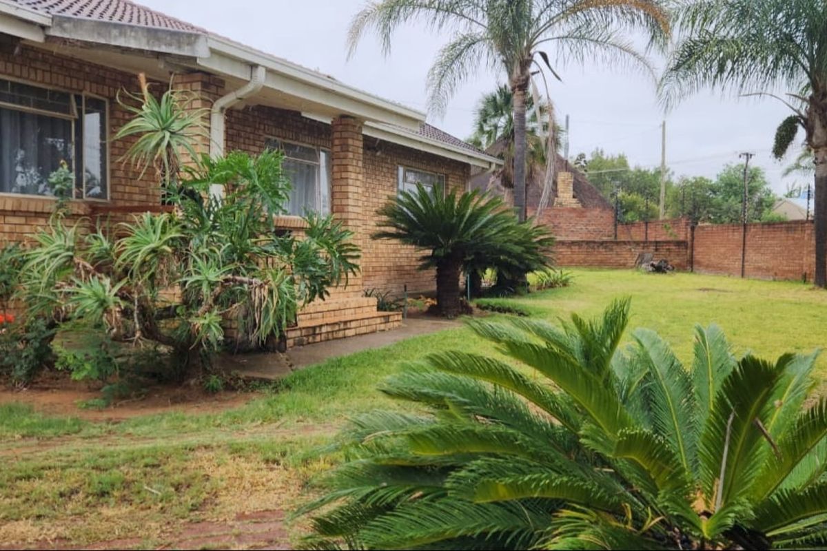 A view of the rear exterior of the house featuring a brick facade, tiled roof, and a spacious garden with a brick boundary wall.