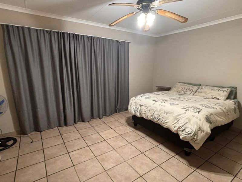 A spacious bedroom featuring neutral tiled flooring, a ceiling fan, and minimalist floating bedside shelves, offering a clean and functional living space.