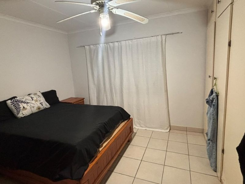 A functional bedroom featuring tiled flooring, a ceiling fan, and built-in cupboards for storage.