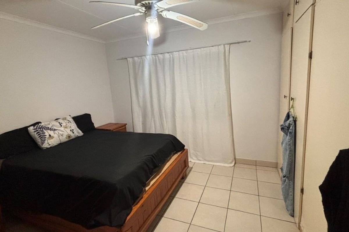 A functional bedroom featuring tiled flooring, a ceiling fan, and built-in cupboards for storage.